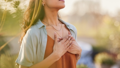 A person stands in nature and breathes intentionally, with their hands on their chest