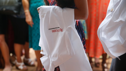 A medical school student carries a white coat with the Rutgers NJMS logo