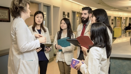 A faculty member talks with pharmacy students in a hospital hallway