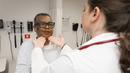 A nursing student examines a patient’s neck in an exam room. 