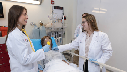 Two students practice clinical skills on a mannequin patient in a simulation lab